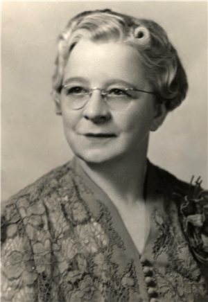 Head and shoulders portrait of a white woman in glasses and a lace dress. 